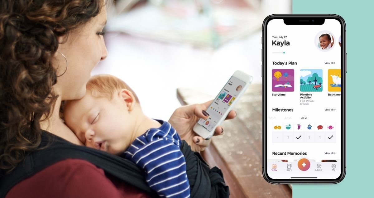 mom looking ParentPal app on her phone while baby sleeps on her chest
