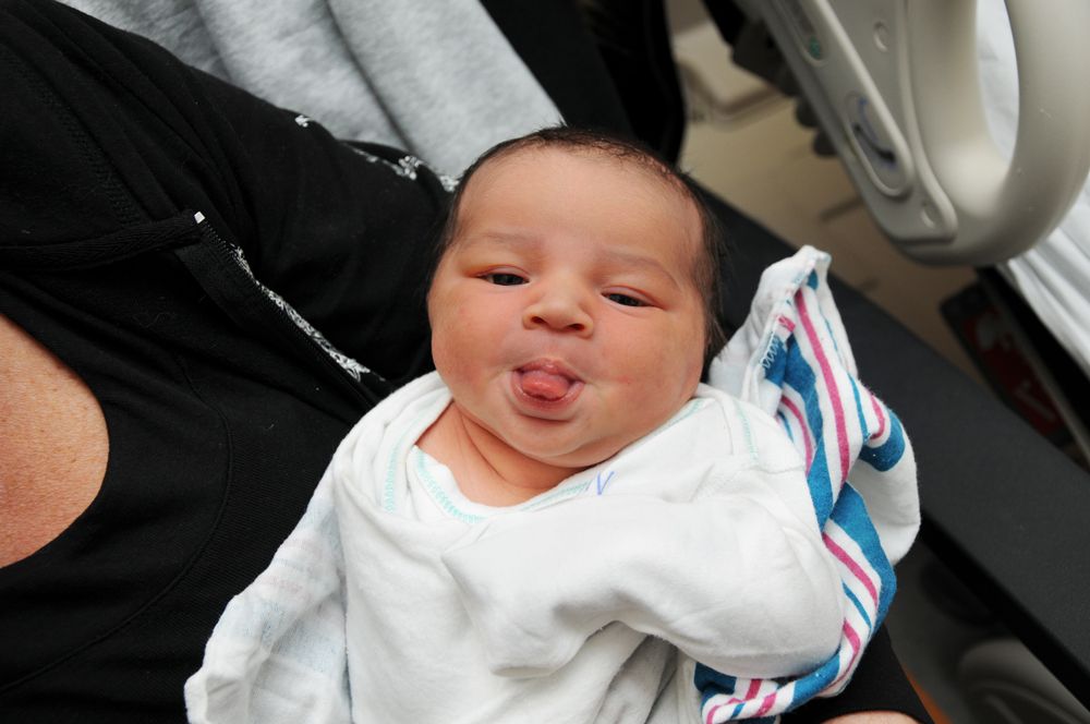 Newborn baby sticking out their tongue while wrapped in a hospital blanket