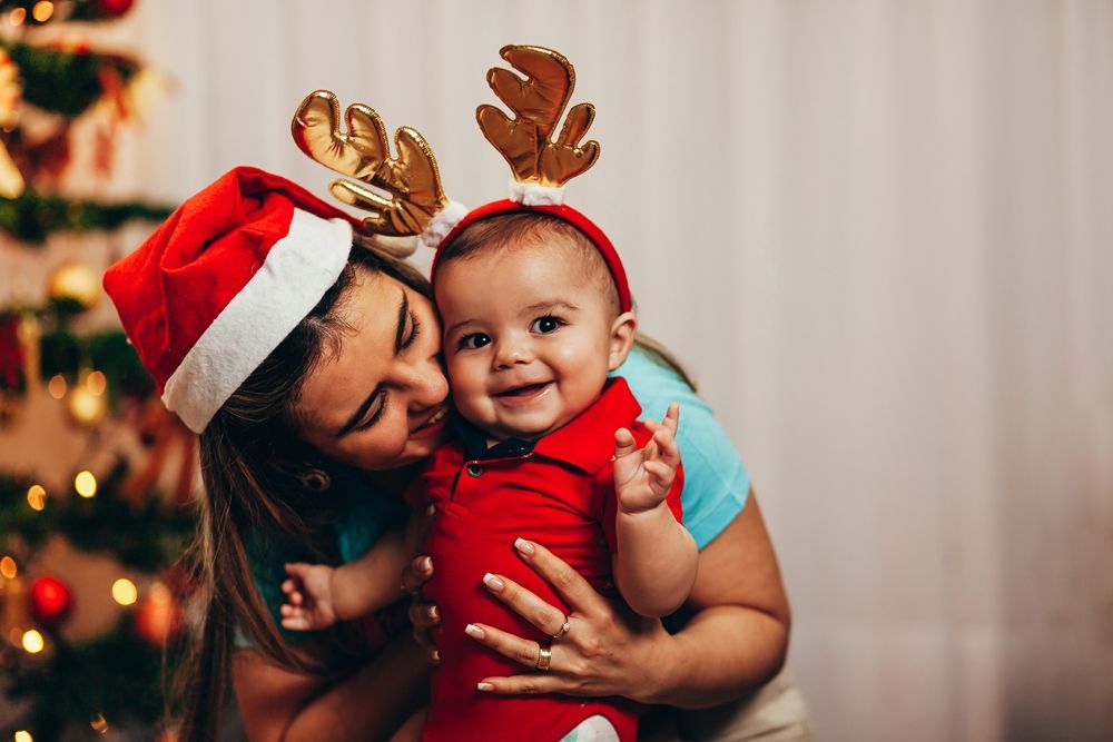 Mom holding baby wearing reindeer antlers for first christmas photo