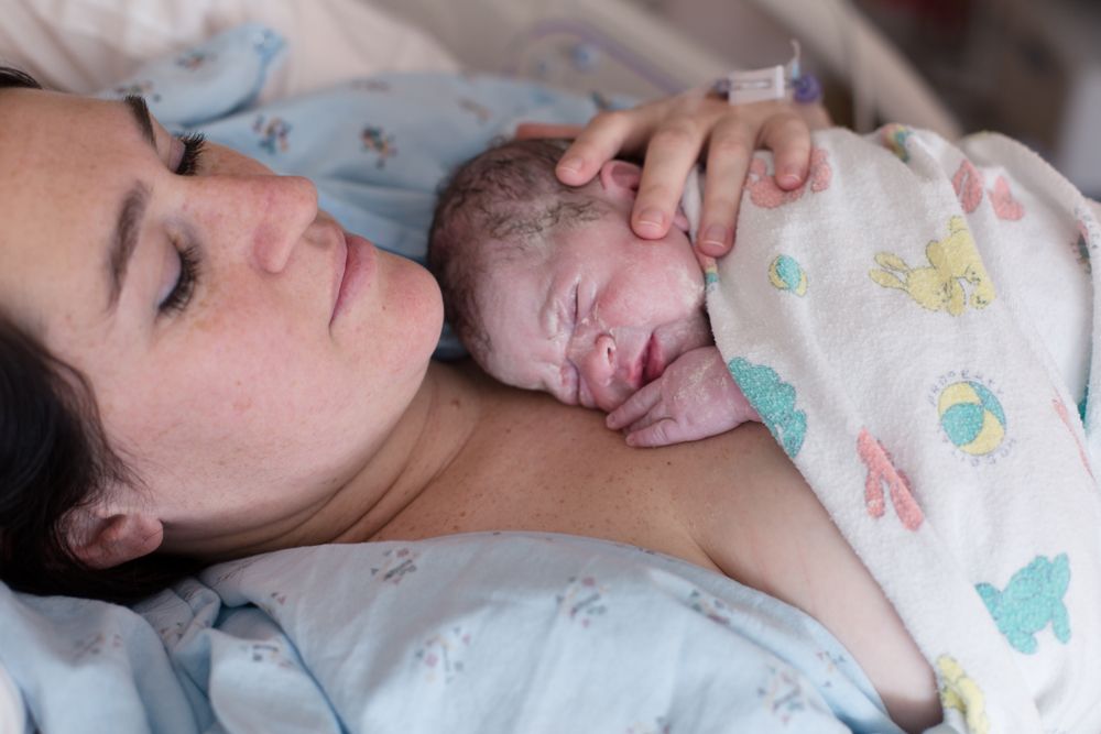 woman after giving birth holding newborn on her chest before she has a shower