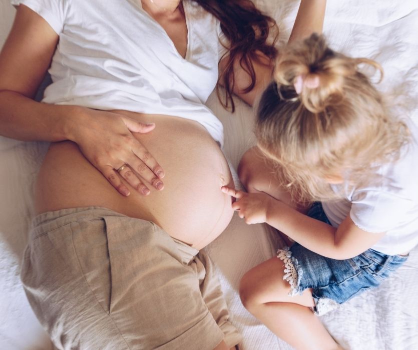 little girl poking her pregnant mother's baby bump
