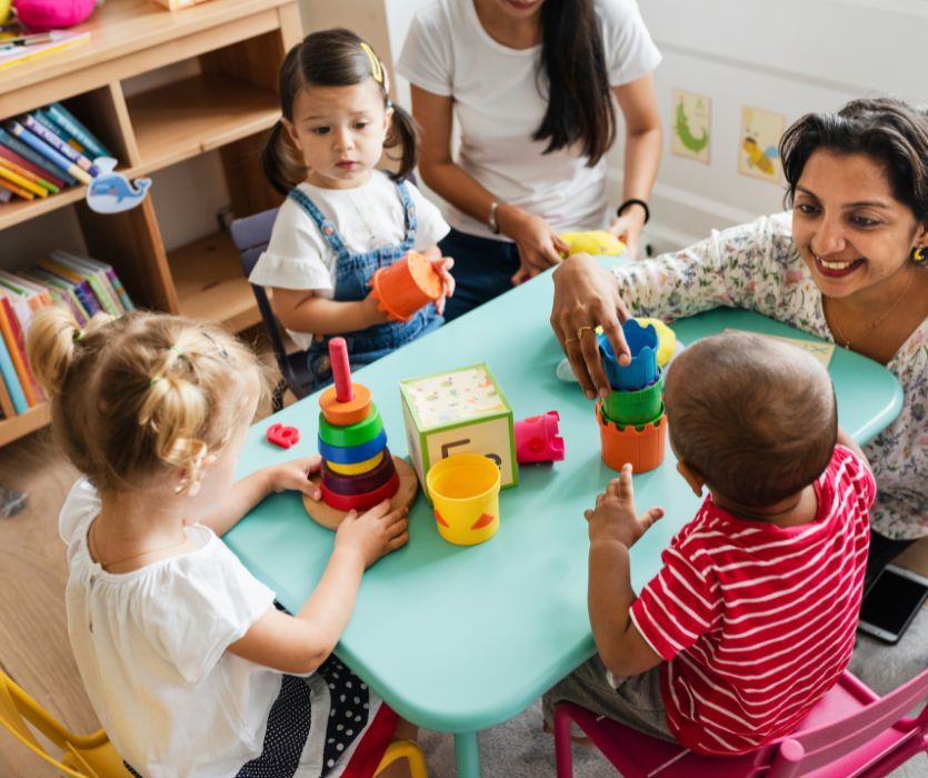 childcare workers playing with kids around a table