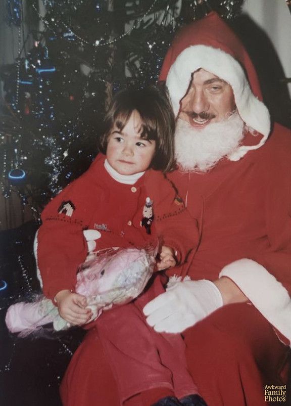 Skeptical child sitting on the lap of a man doing a poor impersonation of Santa.