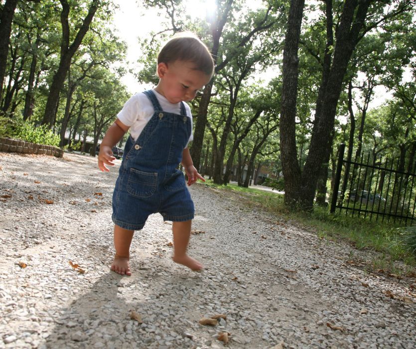 toddler in bare feet walking in a yard with gravel