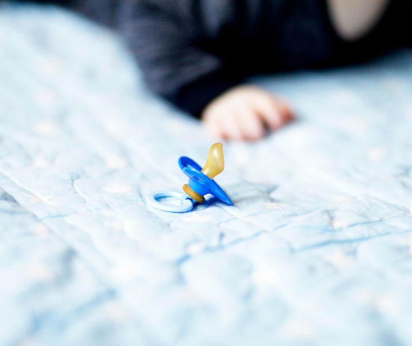 blue baby pacifier with a baby in the background