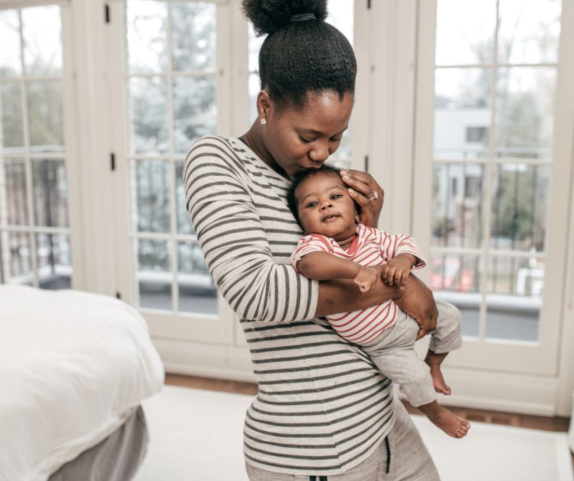 mom holding her baby in front of a window at home