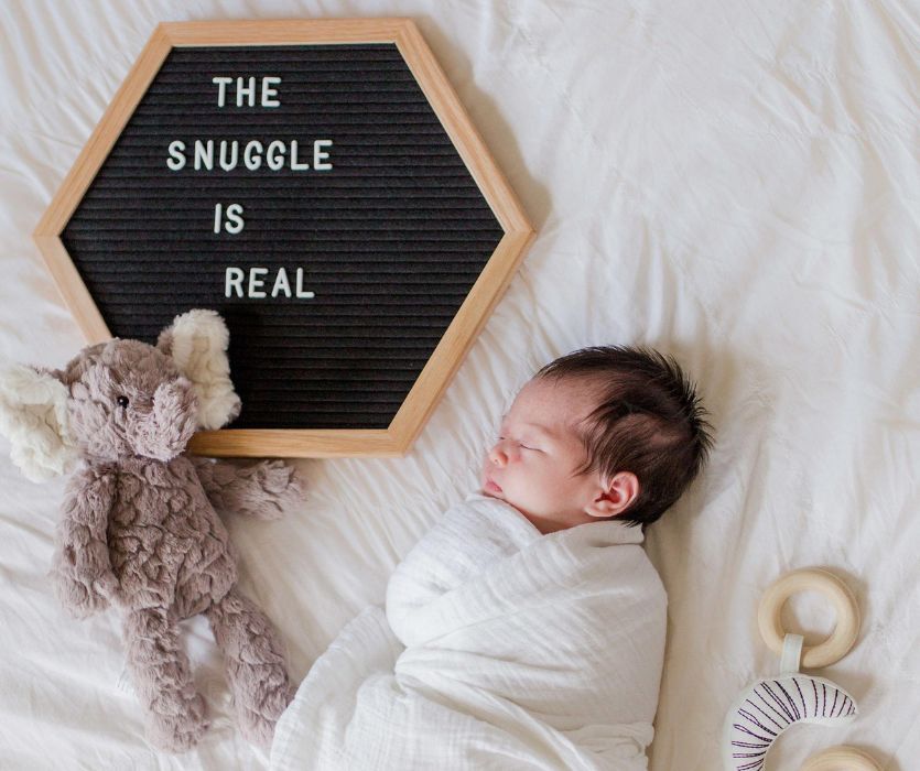 the snuggle is real on a letterboard next to a baby wrapped in a muslin swaddle for instagram