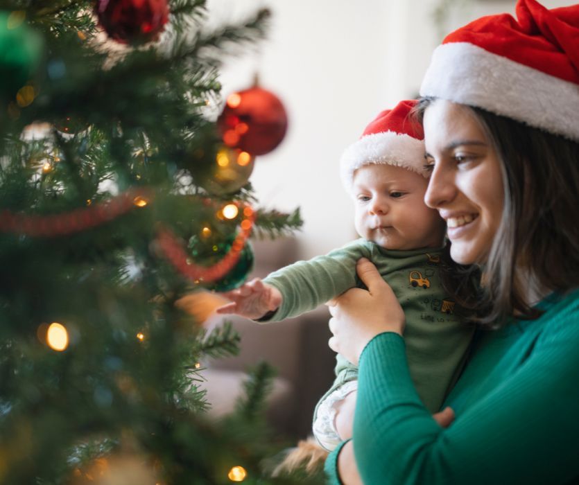 mom holding baby in front of Christmas tree for his first christmas