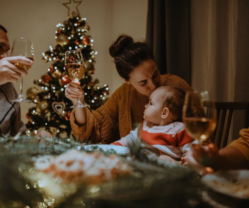 mom at christmas dinner holding a wine glass and kissing her baby on the head