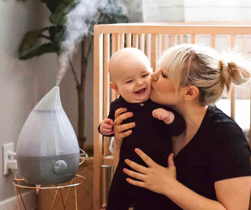 mom kissing her baby with a cold next to a humidifier in the nursery