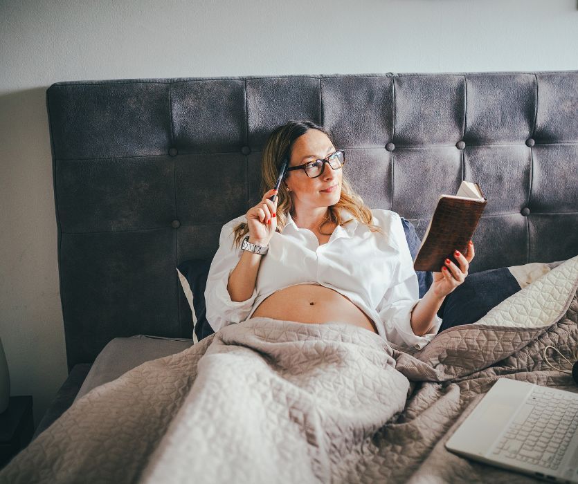 pregnant woman who is a control freak in bed with planner and laptop