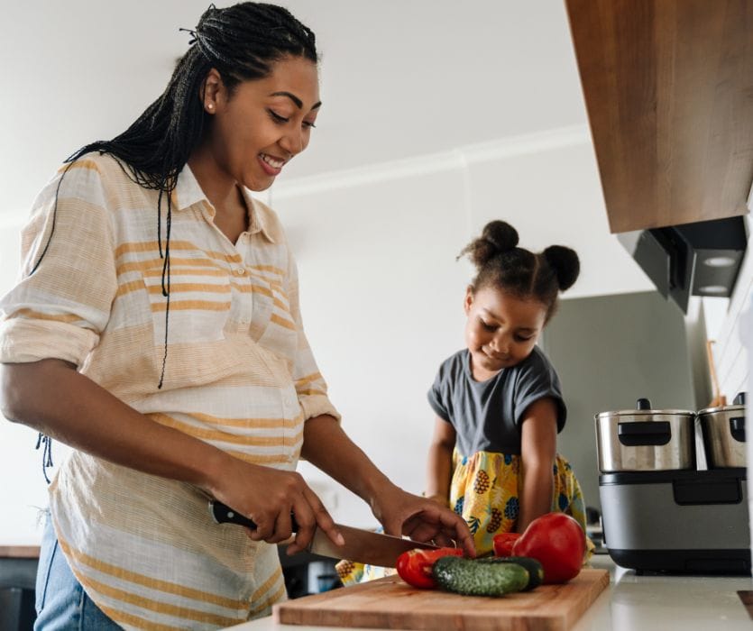 pregnant woman with gestational diabetes cutting vegetables with daughter in the kitchen