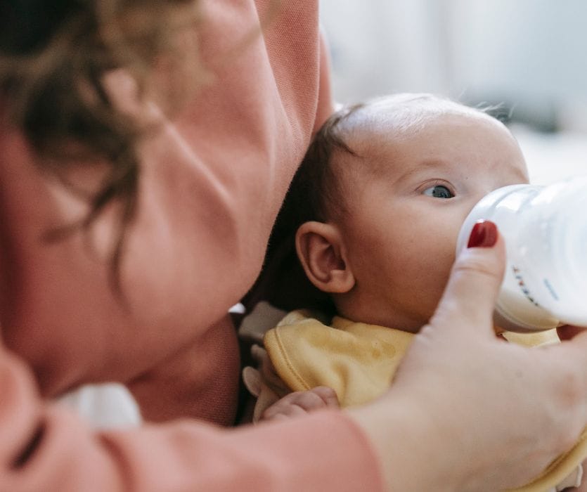 mom feeding her newborn infant organic baby formula in a bottle