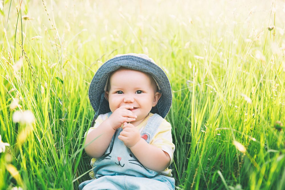 baby with sun protection sitting in grass during the summer
