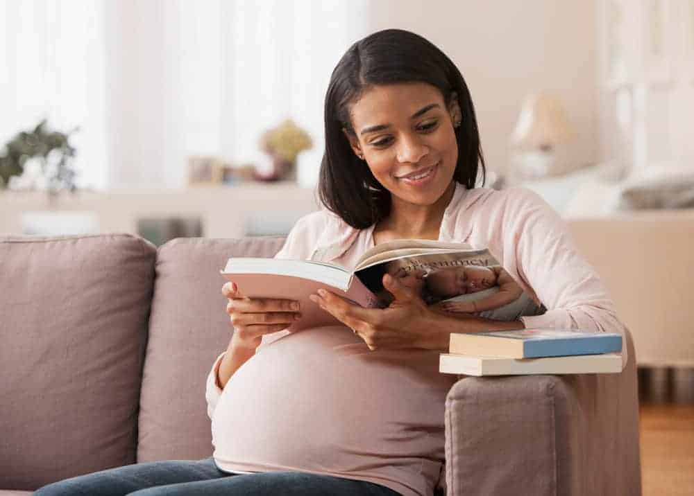 Pregnant woman reading stack of pregnancy books on her couch