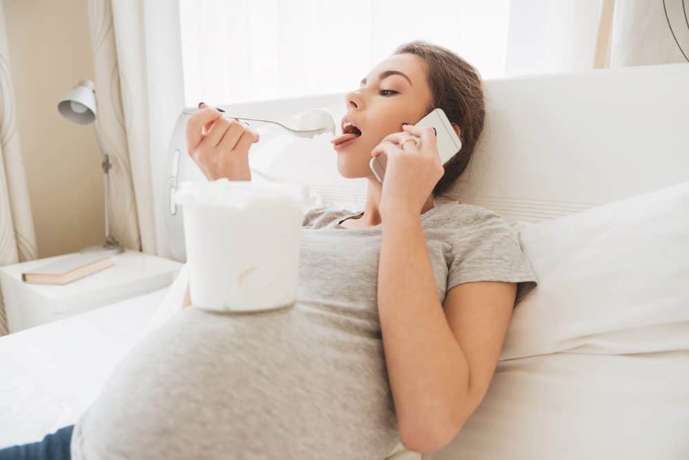Woman eating ice cream off her pregnant belly in her final weeks of pregnancy.