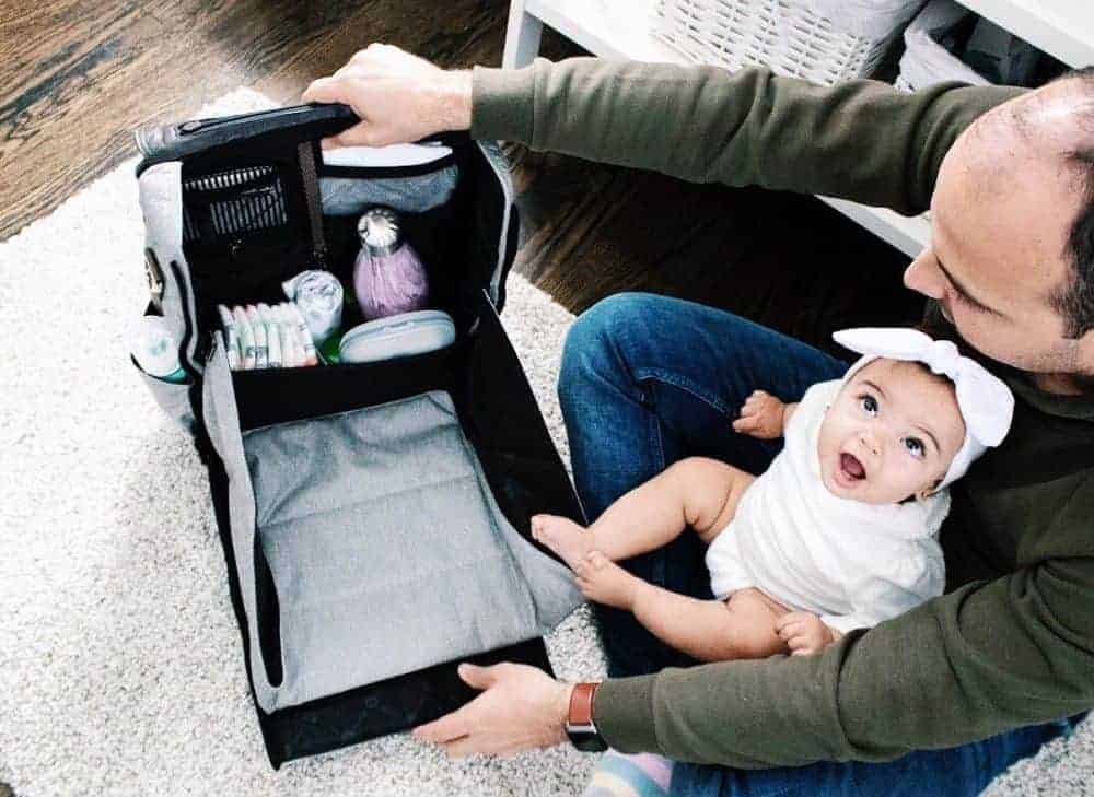 Dad with his daughter on his lap holding a unisex diaper bag open.
