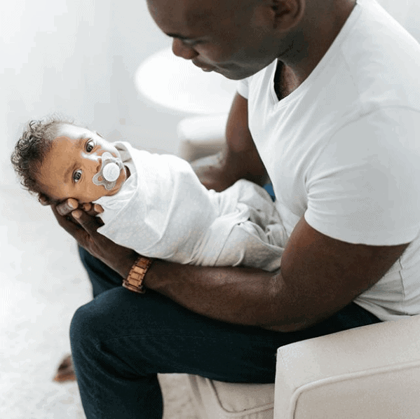 dad holding newborn baby swaddled in a Halo and following the 5Ss.
